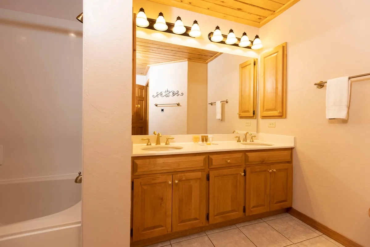 A bright, welcoming bathroom with a double vanity, wooden cabinetry, and a well-lit mirror. The space feels organized and functional, ideal for quick preparations before heading out or freshening up after a day on the slopes.