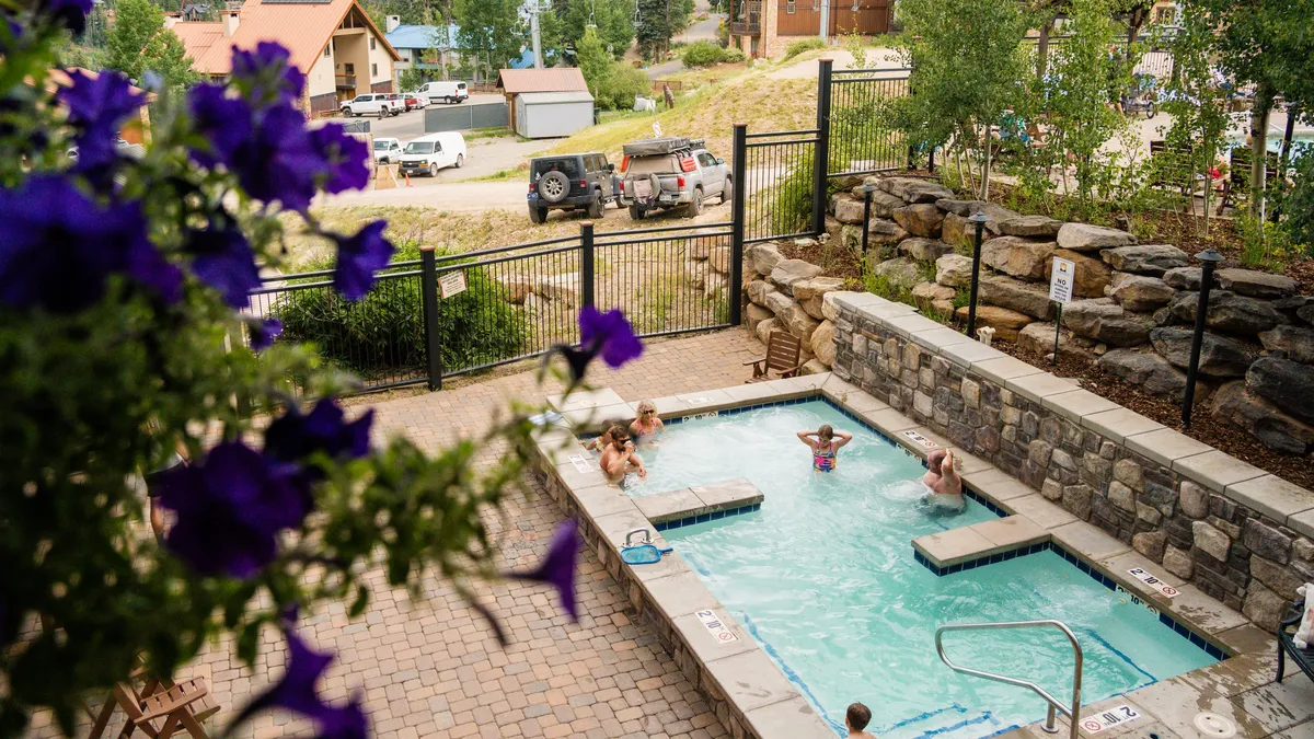 An inviting hot tub nestled among lush landscaping and stone walls, surrounded by greenery and flowering plants. The scene suggests an atmosphere of relaxation and social connection, with the potential for sunset views and tranquil evenings after a day on the slopes.