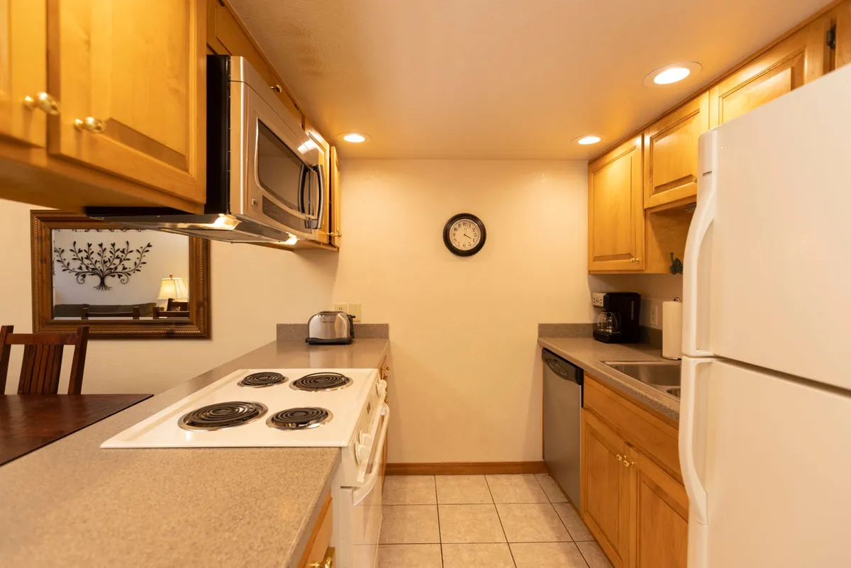 A view that focuses on the kitchen itself, featuring wooden cabinets, modern stainless steel appliances, and a spacious countertop. The scene is functional yet welcoming, highlighting the fully equipped kitchen and practical amenities for preparing meals with ease.