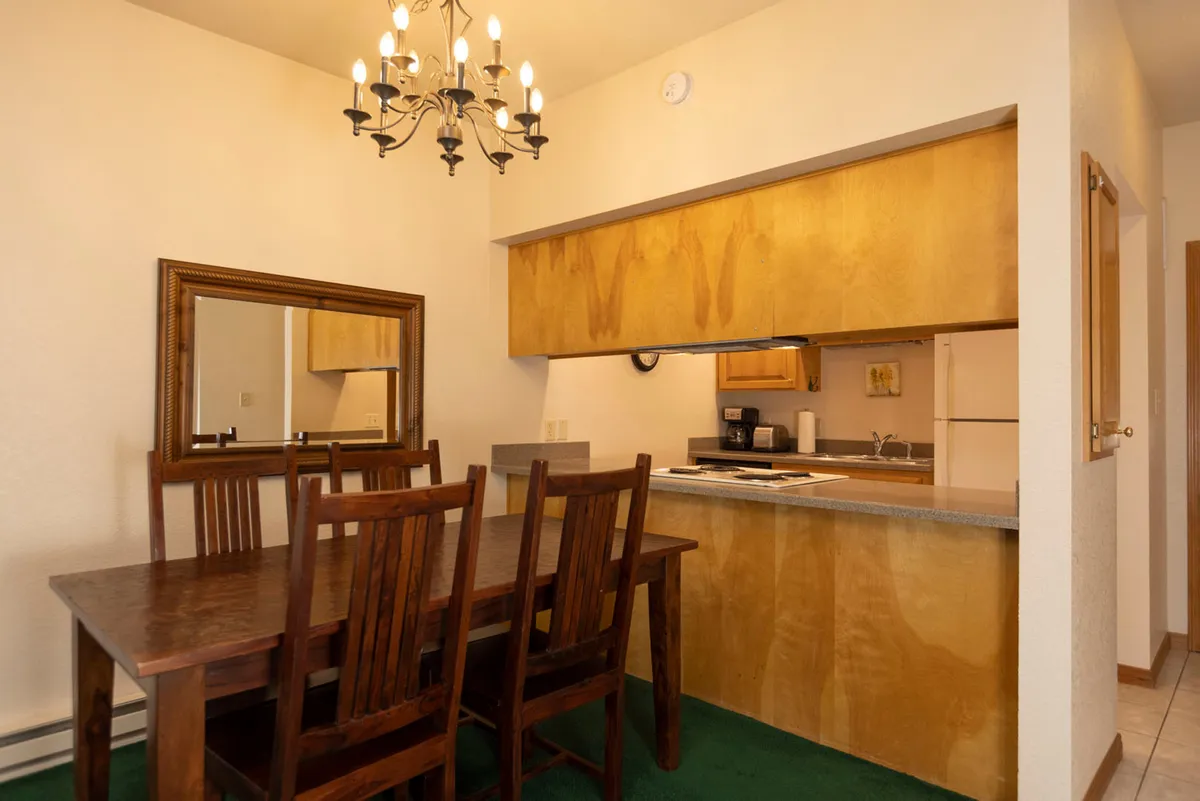 This image showcases the open-concept kitchen and dining area, with a central dining table under a stylish chandelier, adjacent to the kitchen space. The setting is warm and communal, inviting guests to gather for shared meals. The visible modern appliances and thoughtful layout emphasize the ease and comfort of meal preparation.